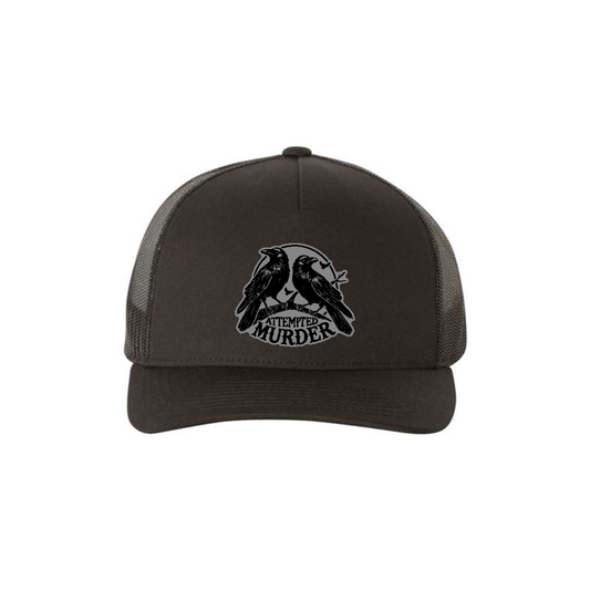 Attempted Murder 5-panel trucker hat in black, front product mockup showing a grey crow design patch.