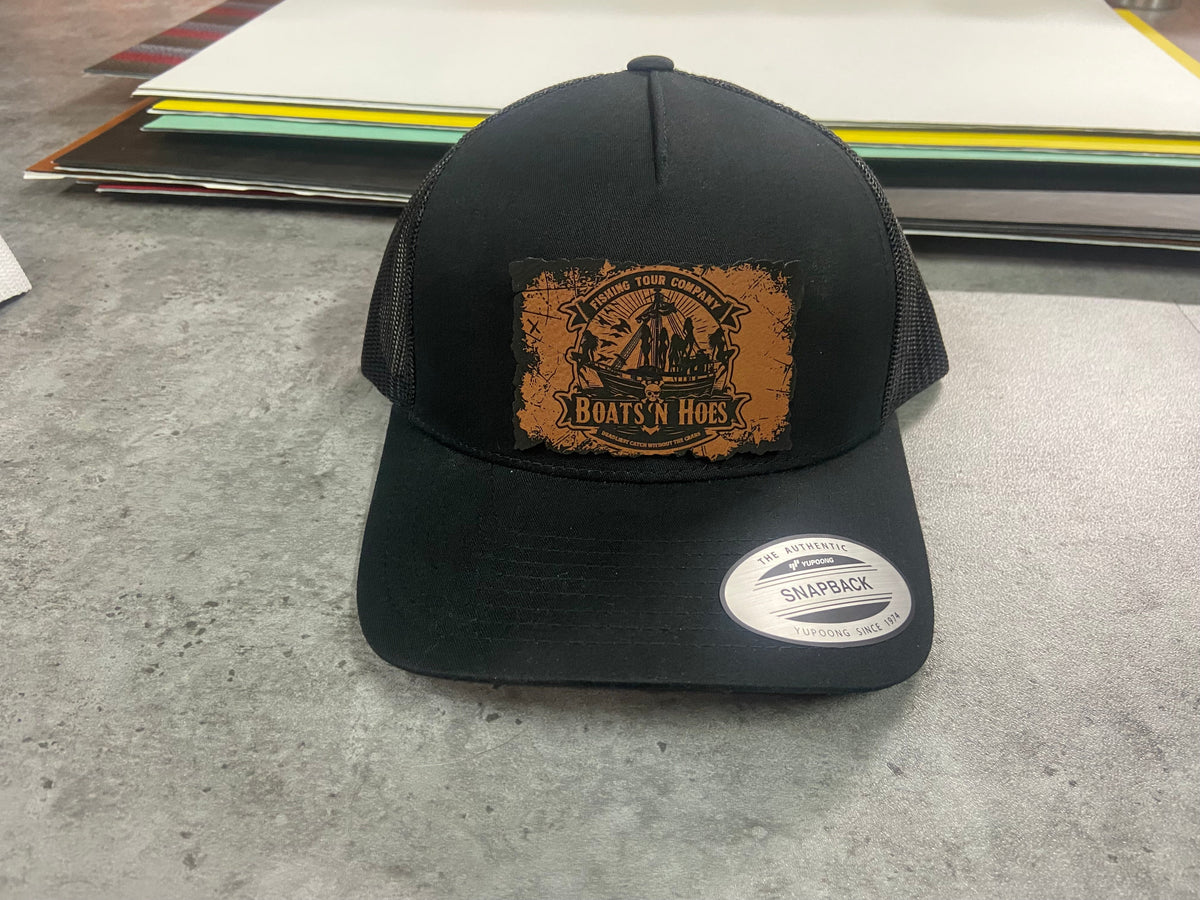 Black Boats & Hoes trucker hat with a rawhide leatherette patch featuring a treasure map design, front view.