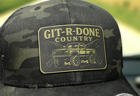 Close-up of the GIT-R-DONE Country engraved patch with off-road truck artwork on a camouflage hat.