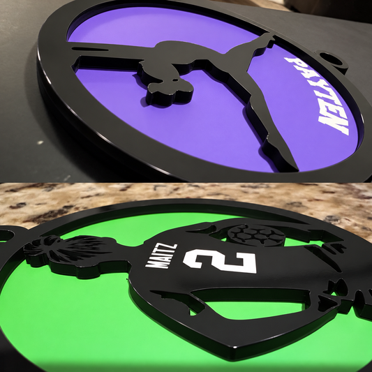 Close-up of purple gymnastics and green volleyball Christmas ornaments showing raised black acrylic silhouettes, coloured bases and personalized lettering.