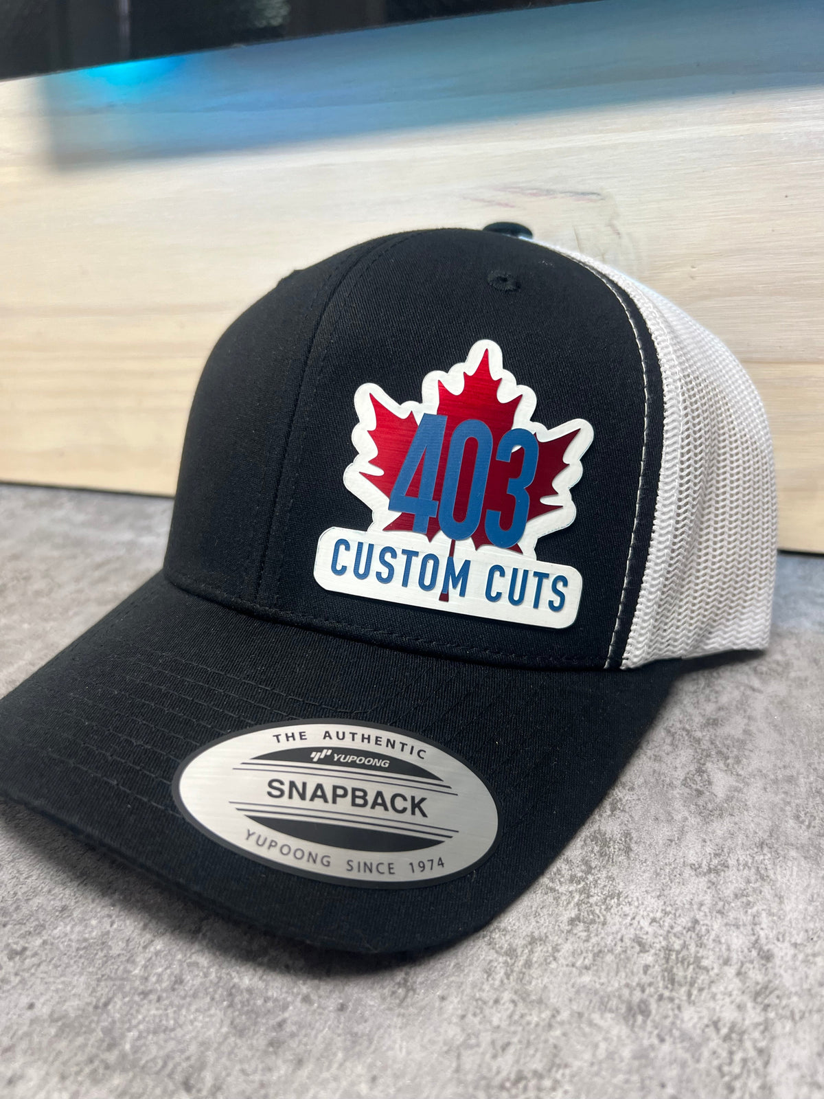 Black and white 403 Custom Cuts trucker hat with a red, white, and blue acrylic maple leaf logo patch, angled view.