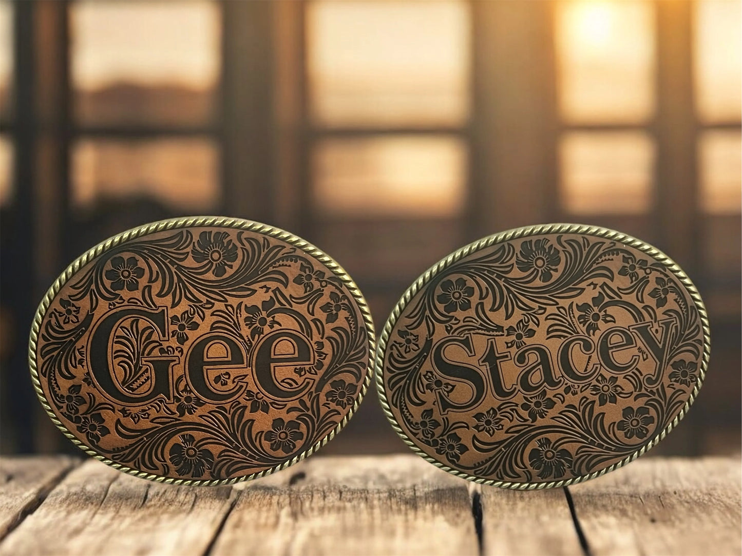 Two ornate belt buckles with 'Gee' and 'Stacey' engraved on a leather patch.