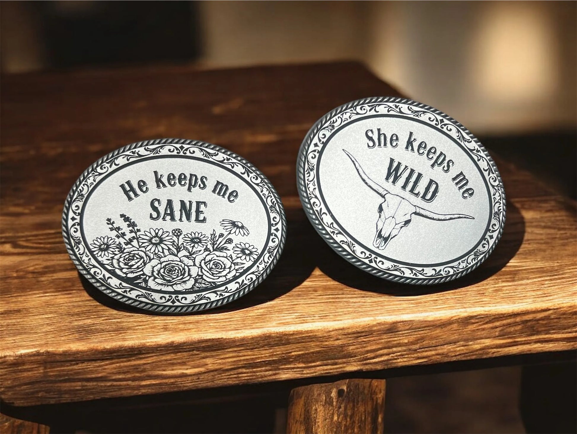 Two round metal belt buckles with engraved leather patches on a wooden surface