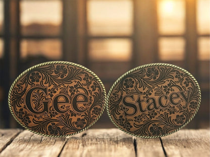 Two ornate belt buckles with 'Gee' and 'Stacey' engraved on a leather patch.