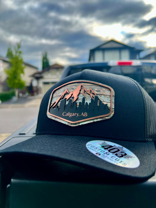 Black Calgary Skyline trucker hat with a shaped cityscape patch featuring mountains and downtown buildings, angled front view.