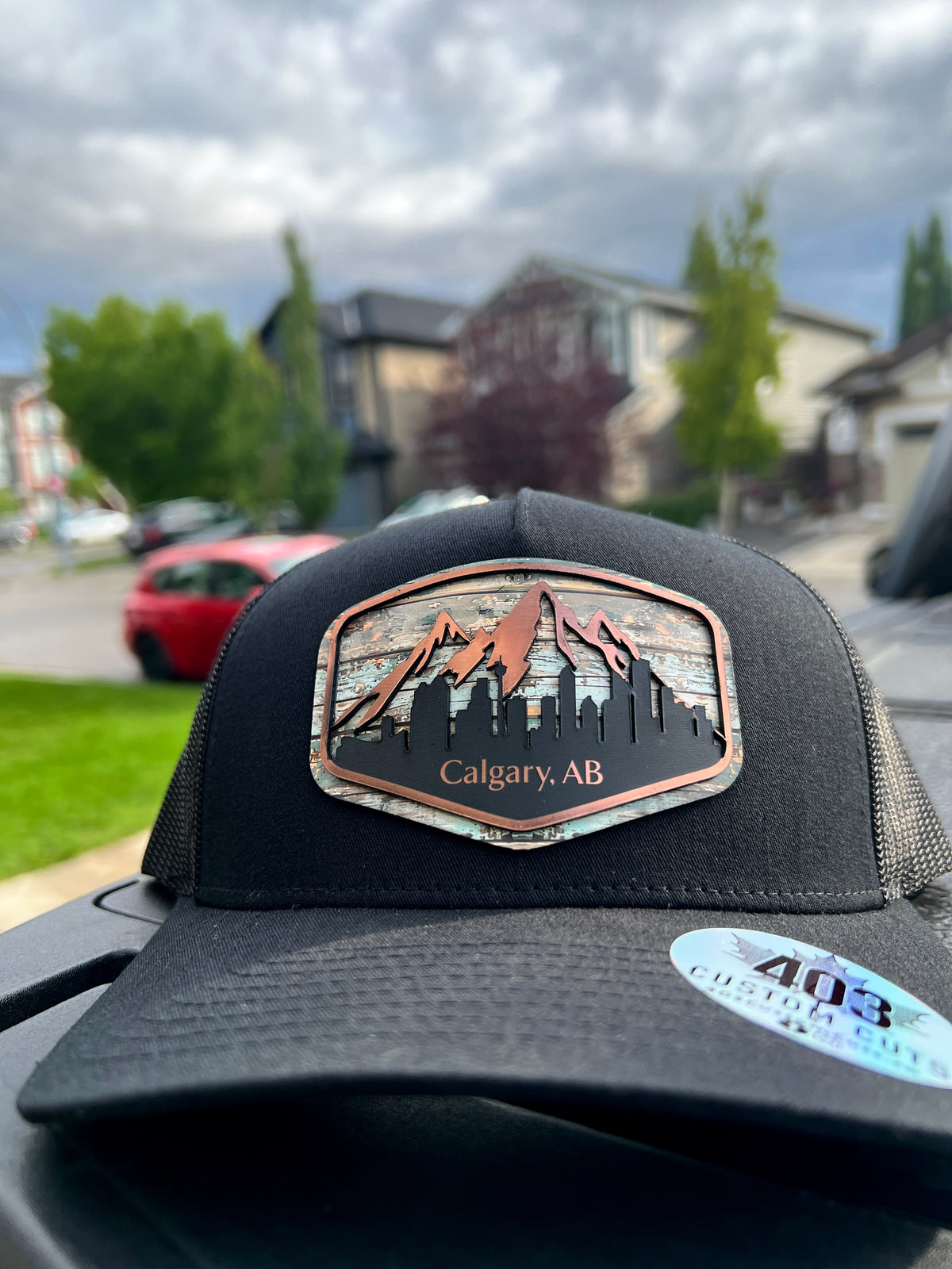 Black Calgary Skyline trucker hat with a mountain and cityscape patch, front view outdoors.