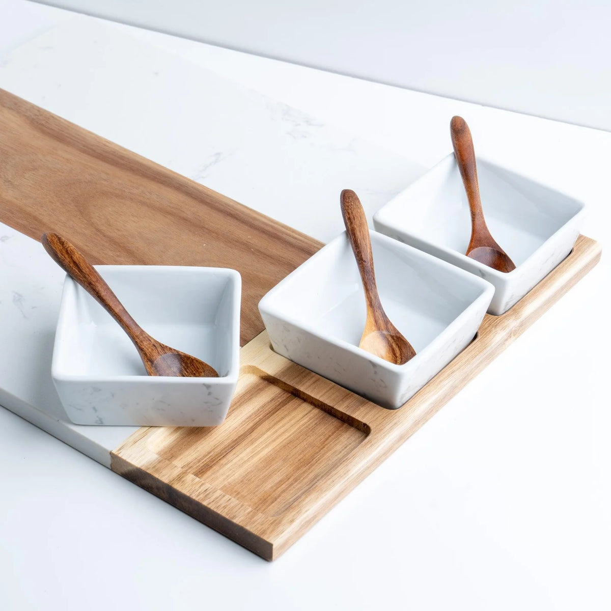 Wooden charcuterie tray with three white dipping bowls and wooden spoons.