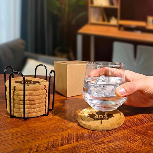 Cork coaster set in a black wire holder beside a drinking glass resting on an engraved coaster.