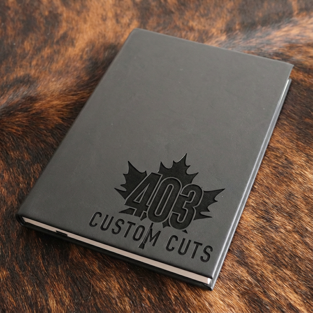 Black leatherette journal with the engraved 403 Custom Cuts maple leaf logo on the cover.