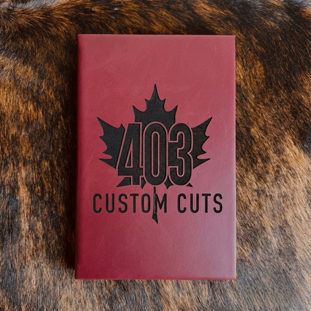 Maroon leatherette journal with the engraved 403 Custom Cuts maple leaf logo on the cover.