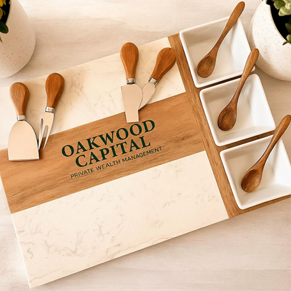 Marble and wood charcuterie board engraved with an Oakwood Capital logo, with serving bowls and utensils.