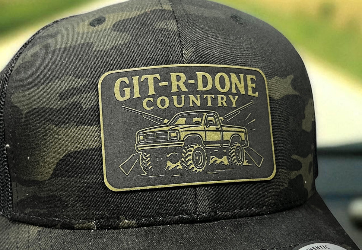 Close-up of the GIT-R-DONE Country engraved patch with off-road truck artwork on a camouflage hat.