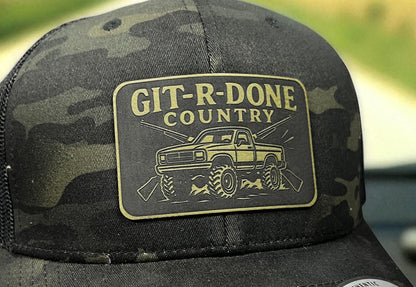 Close-up of the GIT-R-DONE Country engraved patch with off-road truck artwork on a camouflage hat.
