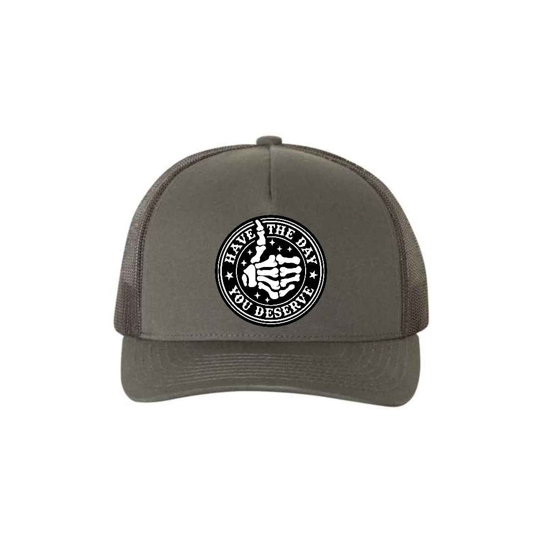 Have the Day You Deserve 5-panel trucker hat in charcoal, front product mockup showing a round engraved slogan patch.