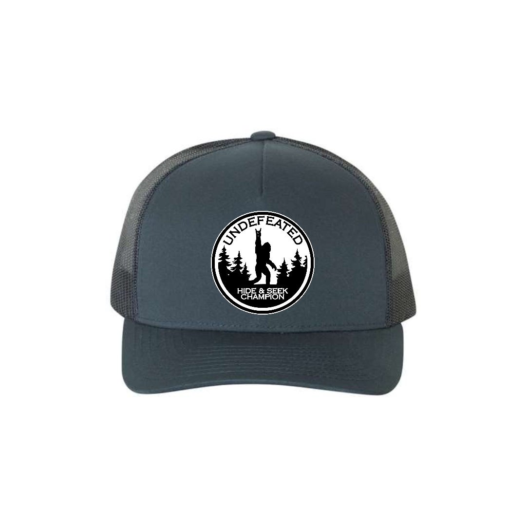 Hide & Seek Champion 5-panel trucker hat in navy, front product mockup showing a round black and white Bigfoot patch.