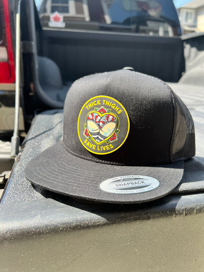 Black Thick Thighs Save Lives trucker hat with a colourful round patch, angled front view on a truck bed.