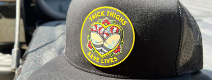 Close-up of the colourful Thick Thighs Save Lives round patch on a black mesh-back trucker hat.
